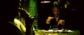 Movie still from “Domino” (2005), directed by Tony Scott – A man sitting at a table in front of a glass of water; Medium shot, High angle