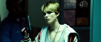 Movie still from “Domino” (2005), directed by Tony Scott – A woman holding a gun while standing next to a wall; Close Up shot, Low angle