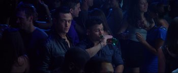 Movie still from “Don Jon” (2013), directed by Joseph Gordon-Levitt – A man drinking a bottle of beer in front of a group of people; Medium shot, High angle
