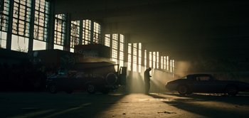 Movie still from “Don't Breathe” (2016), directed by Fede Alvarez – A man standing in a garage with cars in front of a large window; Extreme Wide shot, Low angle