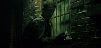 Movie still from “Don't Breathe” (2016), directed by Fede Alvarez – A young man holding a cell phone in front of a brick wall; Close Up shot, Low angle