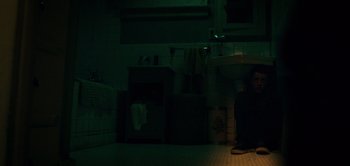 Movie still from “Don't Breathe” (2016), directed by Fede Alvarez – A man sitting in a bathroom under a sink at night; Wide shot, High angle