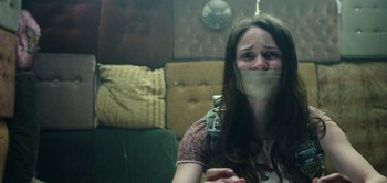 Movie still from “Don't Breathe” (2016), directed by Fede Alvarez – A woman with her mouth taped shut sitting in a room; Close Up shot, Low angle