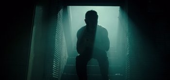 Movie still from “Don't Breathe” (2016), directed by Fede Alvarez – A man sitting on the stairs in the dark; Medium shot, Low angle