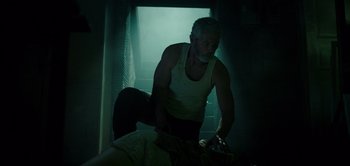 Movie still from “Don't Breathe” (2016), directed by Fede Alvarez – A man in white tank top standing next to a bed; Medium shot, Low angle