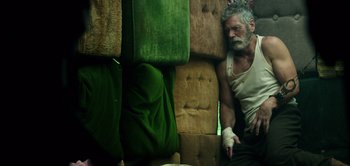 Movie still from “Don't Breathe” (2016), directed by Fede Alvarez – An older man with a bandaged arm rests on a couch; Medium shot, Overhead angle