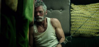Movie still from “Don't Breathe” (2016), directed by Fede Alvarez – An old man with a white beard holding a handcuff; Close Up shot, Overhead angle