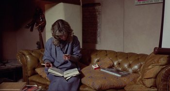 Movie still from “Don't Look Now” (1973), directed by Nicolas Roeg – A woman sitting on top of a couch with a book; Medium shot, High angle
