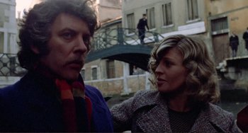 Movie still from “Don't Look Now” (1973), directed by Nicolas Roeg – A man and a woman standing next to each other in front of a bridge; Close Up shot, Low angle