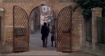 Movie still from “Don't Look Now” (1973), directed by Nicolas Roeg – Two people are walking through an archway in an alley; Wide shot, High angle