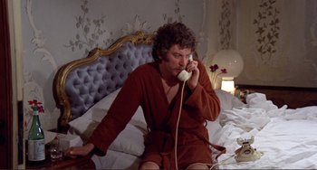 Movie still from “Don't Look Now” (1973), directed by Nicolas Roeg – A man sitting on a bed talking on a phone; Medium shot, High angle