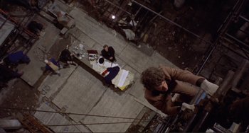 Movie still from “Don't Look Now” (1973), directed by Nicolas Roeg – A group of people sitting on top of a cement floor; Wide shot, Overhead angle