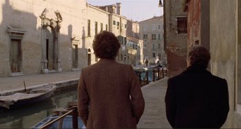 Movie still from “Don't Look Now” (1973), directed by Nicolas Roeg – Two people walking down a street in a city; Wide shot, Over the shoulder angle