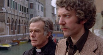 Movie still from “Don't Look Now” (1973), directed by Nicolas Roeg – Two men standing next to each other near a building; Close Up shot, Low angle