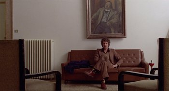 Movie still from “Don't Look Now” (1973), directed by Nicolas Roeg – A man sitting on top of a brown couch in front of a painting; Wide shot, Low angle