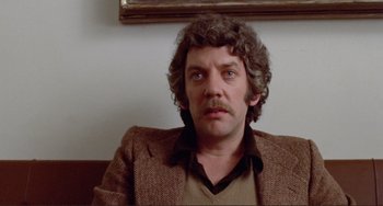 Movie still from “Don't Look Now” (1973), directed by Nicolas Roeg – A person sitting in a chair wearing a brown jacket; Close Up shot, Low angle