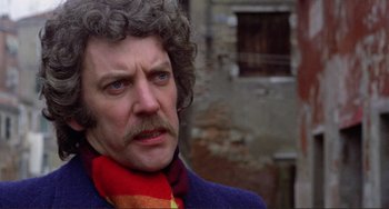Movie still from “Don't Look Now” (1973), directed by Nicolas Roeg – An older man with curly grey hair wearing a red scarf; Close Up shot, Low angle