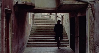 Movie still from “Don't Look Now” (1973), directed by Nicolas Roeg – A man is standing in front of a set of stairs; Wide shot, High angle