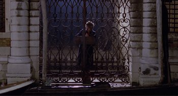 Movie still from “Don't Look Now” (1973), directed by Nicolas Roeg – A man standing in front of a metal gate; Wide shot, High angle