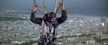 Movie still from “La Grande Vadrouille” (1966), directed by Gérard Oury – A man in a parachute is standing on a building; Wide shot, Low angle