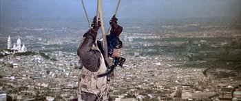 Movie still from “La Grande Vadrouille” (1966), directed by Gérard Oury – A man is flying a parachute over a city; Wide shot, Low angle