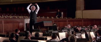 Movie still from “La Grande Vadrouille” (1966), directed by Gérard Oury – An older man is holding his hands up in the air while conducting a orchestra; Medium shot, Low angle