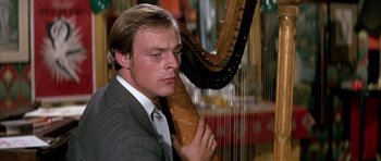 Movie still from “La Grande Vadrouille” (1966), directed by Gérard Oury – A man in a suit and tie holding a harp in front of him; Close Up shot, Low angle