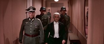 Movie still from “La Grande Vadrouille” (1966), directed by Gérard Oury – A group of men standing next to each other in a hallway; Medium shot, Over the shoulder angle