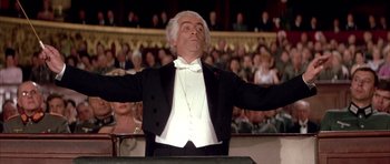 Movie still from “La Grande Vadrouille” (1966), directed by Gérard Oury – A man in a tuxedo is standing in front of an audience with his arms outstretched; Medium shot, Low angle
