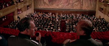 Movie still from “La Grande Vadrouille” (1966), directed by Gérard Oury – Two men are sitting in front of an orchestra; Extreme Wide shot, High angle