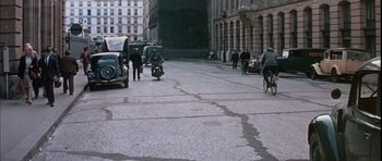 Movie still from “La Grande Vadrouille” (1966), directed by Gérard Oury – A man riding a motorcycle down the middle of a street; Extreme Wide shot, High angle