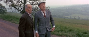 Movie still from “La Grande Vadrouille” (1966), directed by Gérard Oury – Two men in suits and hats standing next to each other on a field; Medium shot, Over the shoulder angle
