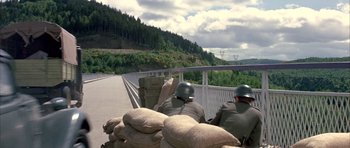 Movie still from “La Grande Vadrouille” (1966), directed by Gérard Oury – Two men in helmets are standing on a bridge over a river; Wide shot, High angle