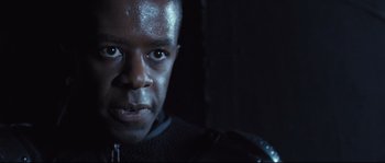 Movie still from “Doomsday” (2008), directed by Neil Marshall – A person wearing a suit and looking at the camera; Close Up shot, Over the shoulder angle