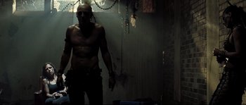 Movie still from “Doomsday” (2008), directed by Neil Marshall – A man with a gun in a dark room with chains hanging from the ceiling; Medium shot, Low angle