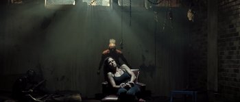Movie still from “Doomsday” (2008), directed by Neil Marshall – A woman sitting on a chair next to a man in chains; Wide shot, Over the shoulder angle