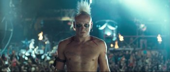 Movie still from “Doomsday” (2008), directed by Neil Marshall – A man with a white mohawk is standing in front of a crowd of people; Close Up shot, Low angle