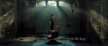 Movie still from “Doomsday” (2008), directed by Neil Marshall – A person standing in a room with a chair; Wide shot, Low angle