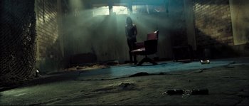 Movie still from “Doomsday” (2008), directed by Neil Marshall – A person standing in a room with a chair; Wide shot, High angle