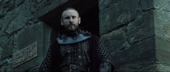 Movie still from “Doomsday” (2008), directed by Neil Marshall – A man in a leather outfit standing in front of a stone wall; Medium shot, Low angle