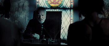 Movie still from “Doomsday” (2008), directed by Neil Marshall – An older man sitting in front of a stained - glass window; Medium shot, Over the shoulder angle