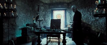 Movie still from “Doomsday” (2008), directed by Neil Marshall – A man standing in front of a table in a room with stained glass; Wide shot, Low angle