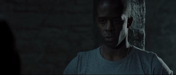 Movie still from “Doomsday” (2008), directed by Neil Marshall – A black man with a white mask in a dark room; Close Up shot, Over the shoulder angle