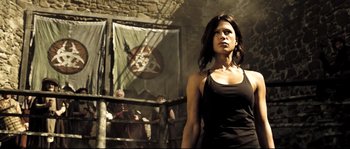 Movie still from “Doomsday” (2008), directed by Neil Marshall – A woman standing in front of a wall with a flag; Medium shot, Low angle