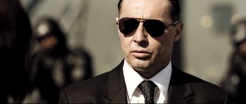 Movie still from “Doomsday” (2008), directed by Neil Marshall – A person wearing a suit and sunglasses; Close Up shot, Low angle