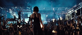 Movie still from “Doomsday” (2008), directed by Neil Marshall – A woman in a black outfit standing in front of an audience; Wide shot, Low angle