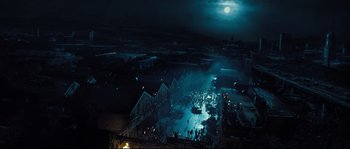 Movie still from “Doomsday” (2008), directed by Neil Marshall – An aerial view of a city at night with a full moon in the background; Extreme Wide shot, High angle
