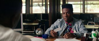 Movie still from “Dope” (2015), directed by Rick Famuyiwa – A man sitting at a table holding a card; Close Up shot, Over the shoulder angle