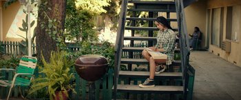 Movie still from “Dope” (2015), directed by Rick Famuyiwa – A woman sitting on the steps of a house reading; Wide shot, High angle