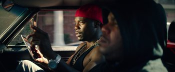 Movie still from “Dope” (2015), directed by Rick Famuyiwa – A man in a red hat and a man in a black tank top driving a car; Close Up shot, Over the shoulder angle
